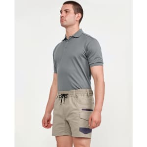A man wearing a grey polo shirt and beige stretch drill work shorts with a logo. The shorts feature side pockets.