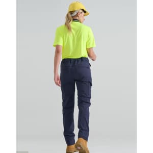 A woman wearing a bright yellow shirt and navy flexi work pants, seen from the back, with a cap and boots.