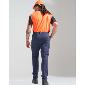 A man wearing orange and black work attire stands with his back to the camera, sporting navy blue flexi work pants and a helmet.