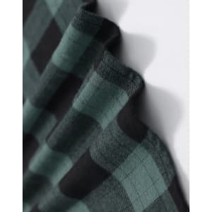 A close-up of a unisex flannel shirt in black and green plaid fabric, featuring a logo.