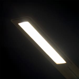 A sleek, rectangular LED lamp emits a bright, white light against a dark background. The lamp has a minimalist design.