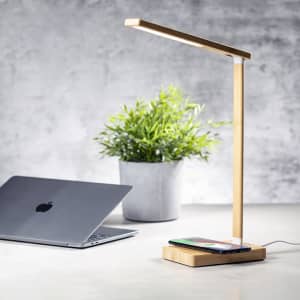 A sleek bamboo lamp with a wireless charging base, beside a laptop and a potted plant.