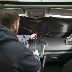 A black sunshade is being set up inside a car, with a person adjusting it in the front seat.