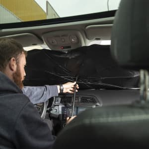 A black sunshade being installed inside a car, with a person reaching to adjust it.