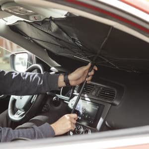 A black sunshade being installed in a car's interior, covering the windshield. It has a sleek design and a sturdy handle.