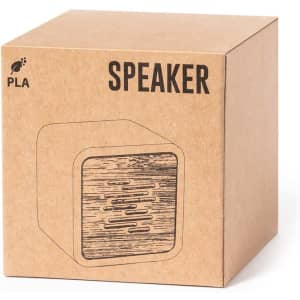 A brown cardboard box containing a wooden-textured speaker. The box features a logo and the word "SPEAKER."