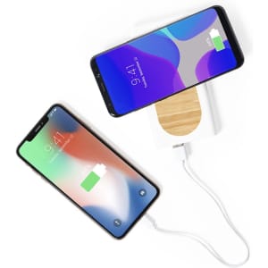 A white power bank with a bamboo top is charging two smartphones, one green and one black.