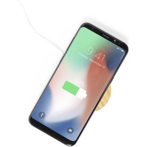 A wireless charger in a circular design with a wooden base, supporting a smartphone displaying a battery charge indicator.