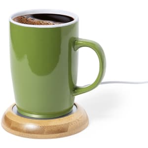 A green mug filled with coffee seated on a circular bamboo cup warmer. The cup has a handle and is plugged in.