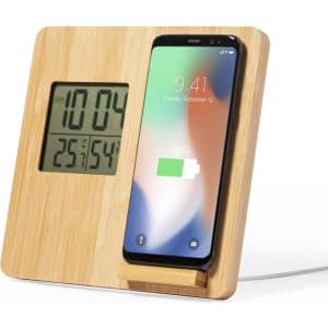 A bamboo wireless charger with a built-in clock, displaying time and temperature, and a phone charging beside it.