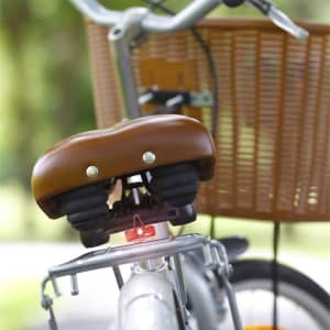 A brown bicycle saddle with a red safety light attached, positioned near a wicker bike basket.