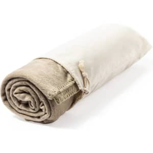 A rolled blanket in beige and cream, featuring a soft texture and tied with a cord. It has a branding logo.