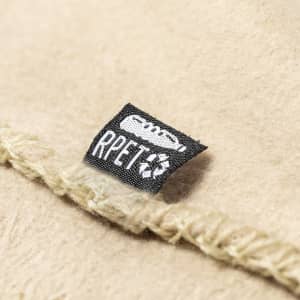 A beige blanket with a textured edge and a small tag featuring a logo and recycling symbol.