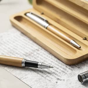 A bamboo pen set featuring a silver clip and a bamboo casing, placed on textured paper. Includes a logo on the packaging.