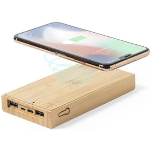 A power bank in a bamboo finish with multiple USB ports and a phone wirelessly charging above it.