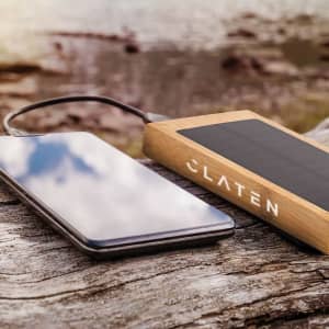 A power bank with a wooden exterior and solar panel, positioned next to a smartphone on a rustic wooden surface.