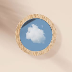 A round pocket mirror with a wooden frame reflecting a blue sky and a white cloud.