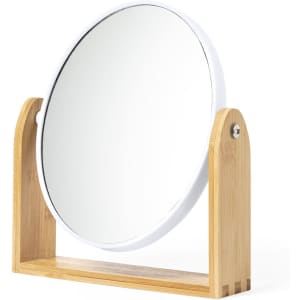 A round mirror with a white frame, supported by a natural bamboo stand.