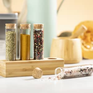 A spice set featuring glass tubes with cork stoppers, containing various spices and displayed on a bamboo holder.