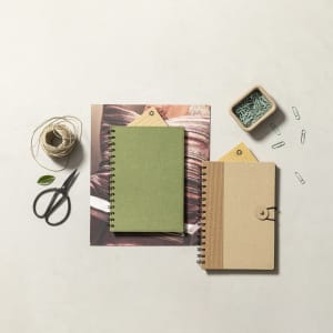 A green notebook and a brown spiral-bound notebook on a neutral surface, accompanied by scissors, twine, and paper clips.