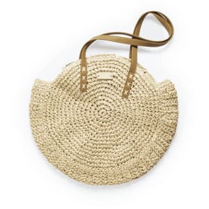 A round, woven straw tote bag with brown straps and a logo. Its natural colour adds a chic touch.