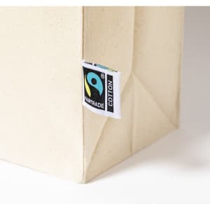 A beige tote bag made of cotton with a Fairtrade label attached. The bag has structured sides.