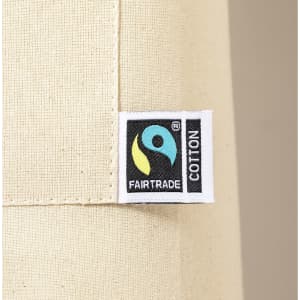 A natural-coloured apron featuring a Fairtrade label, made of cotton. The fabric is smooth with a simple design.
