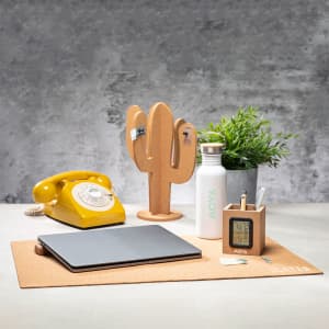 A yellow retro phone, a cork cactus, a stainless steel drink bottle, a green plant, and a laptop on a cork desk mat.