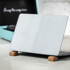 A laptop on a wooden stand, featuring a sleek, silver finish, with a turquoise box in the background.