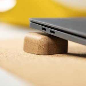 A cork phone holder supporting a laptop, showcasing a grey device with USB ports.