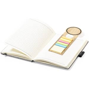 A wooden ruler bookmark with multiple coloured tabs resting on an open lined notebook.