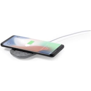 A wireless charger in grey with a smartphone placed on it, displaying a charging icon.