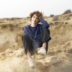 A casual navy blue sweatshirt worn by a person seated on rocky terrain, paired with black trousers and white sneakers.