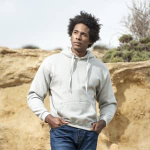 A grey adult hooded sweatshirt is worn by a man in a natural outdoor setting, featuring a simple logo.