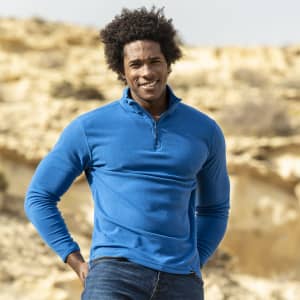 A blue polar fleece jacket with a half-zip collar, worn by a smiling man against a natural landscape.