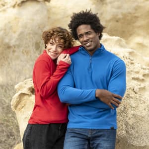 A red polar fleece jacket and a blue polar fleece jacket on two models smiling against a rocky background.