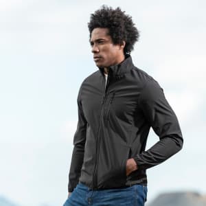 A black soft shell jacket worn by a model outdoors, featuring a zipped front and a logo.