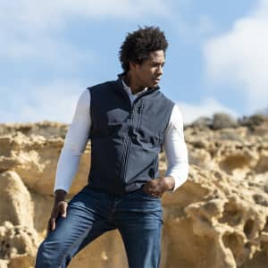 A man is wearing a navy Jandro Vest over a white long-sleeve shirt, posed against a rocky landscape.