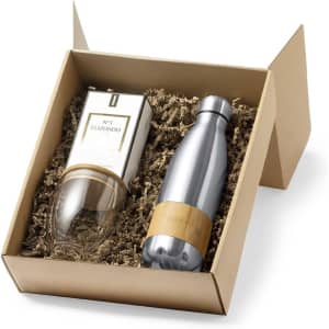 A gift box containing a silver drink bottle and a glass with a wooden base, nestled in brown packing material.