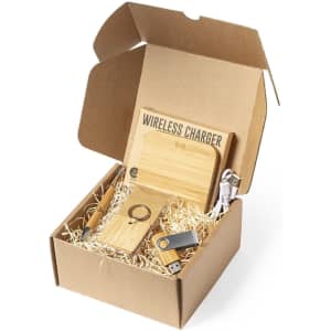 A gift box containing a wooden wireless charger, USB drive, keyring, and cables, all resting on shredded paper.