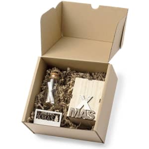 A gift box containing a wooden hourglass and decorative pieces with a Christmas theme, filled with crinkle paper.