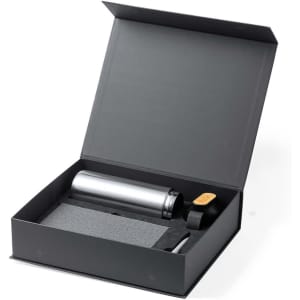 A gift set in a black box containing a silver drink bottle, a black cap, and a grey notebook.