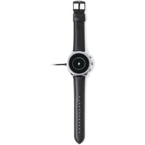 A black smart watch with a round face and silver accents, featuring a charging icon on the display and a logo on the strap.