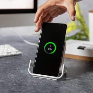 A wireless charger in white, holding a smartphone displaying a charging indicator.