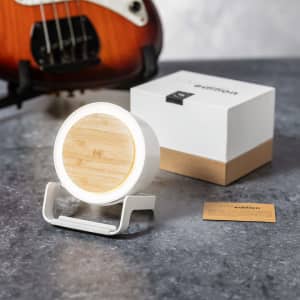 A white multifunction lamp with a bamboo top, accompanied by a box and a card. It is set against a textured grey surface.