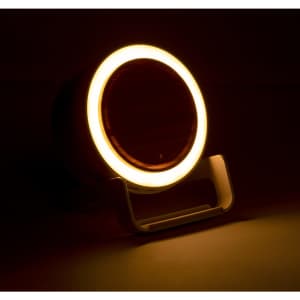 A multifunction lamp with a circular design, featuring a warm glow and a stand, in a dark setting.