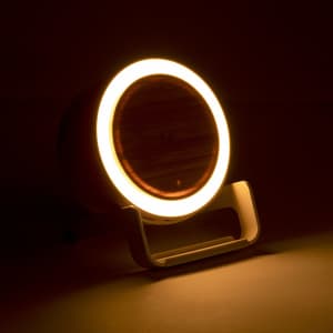 A multifunction lamp with a circular design, featuring a warm glow and a wooden accent on a white stand.
