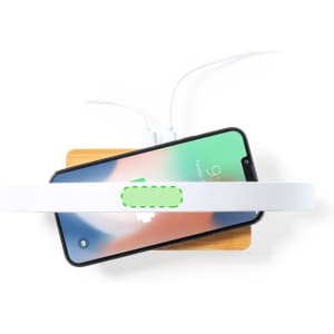 A wireless charger lamp in white, positioned above a smartphone on a wooden surface, with charging cables visible.