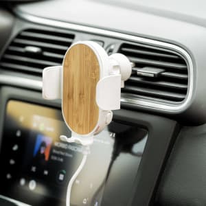 A wireless charger holder with a bamboo finish, mounted on a car air vent, next to a car display screen.