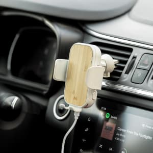 A wireless charger holder with a bamboo finish, mounted in a car's air vent, connected to a smartphone.